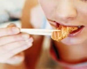 Primer plano de una persona joven disfrutando de un bocado de salmón marinado o sushi, utilizando palillos de madera. La imagen resalta el consumo de pescado de forma saludable y moderna, asociando productos marinos frescos con hábitos alimenticios equilibrados entre la población joven.