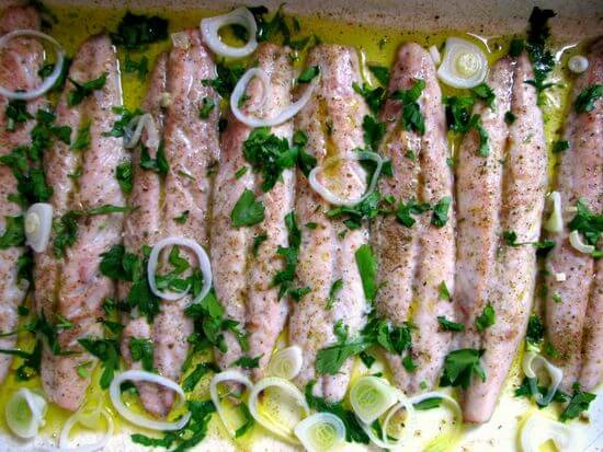 Varios filetes de caballa (xarda) dispuestos de forma vertical en una bandeja de horno, bañados en aceite de oliva y sazonados con especias. El pescado está cubierto con abundantes aros de cebolleta fresca y perejil picado, resaltando una preparación saludable, sencilla y llena de sabor mediterráneo.