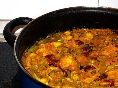 Una deliciosa fideuá de rape cocinada directamente en una cazuela azul de borde negro. El plato presenta fideos cortos entrelazados con trozos de rape, pimiento verde picado y un sofrito de color intenso y meloso, resaltando la textura jugosa de esta receta tradicional marinera.