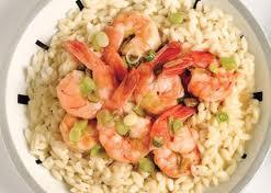 Un plato de arroz meloso o risotto servido en un cuenco blanco, coronado con varias colas de langostinos salteadas que aportan un vibrante color rosado. El plato está decorado con cebolleta fresca picada, que añade un toque verde y crujiente a la textura suave del arroz, creando una combinación elegante y apetitosa.