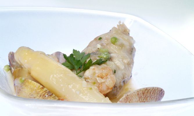 Un delicado lomo de bertorella cocinado en una suave salsa verde, acompañado de un espárrago blanco grueso, almejas y un langostino pelado. El plato, de estilo minimalista y elegante sobre un fondo blanco, está decorado con guisantes y una ramita de perejil fresco, resaltando los sabores del mar con una presentación sofisticada.
